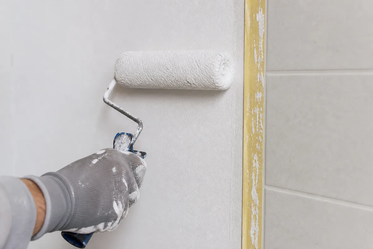 Mur en cours de peinture au rouleau à côté d&rsquo;un carrelage fraîchement posé
