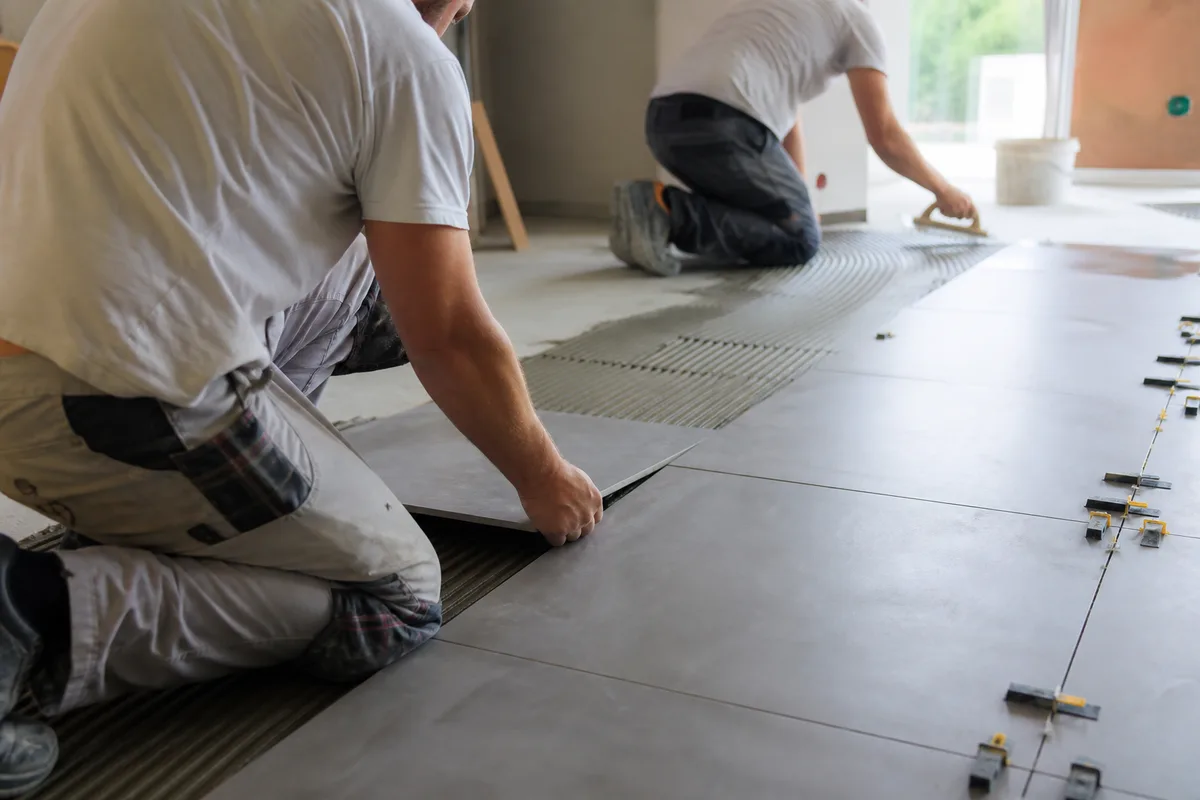 Deux carreleurs professionnels posant du carrelage grand format dans une pièce en chantier