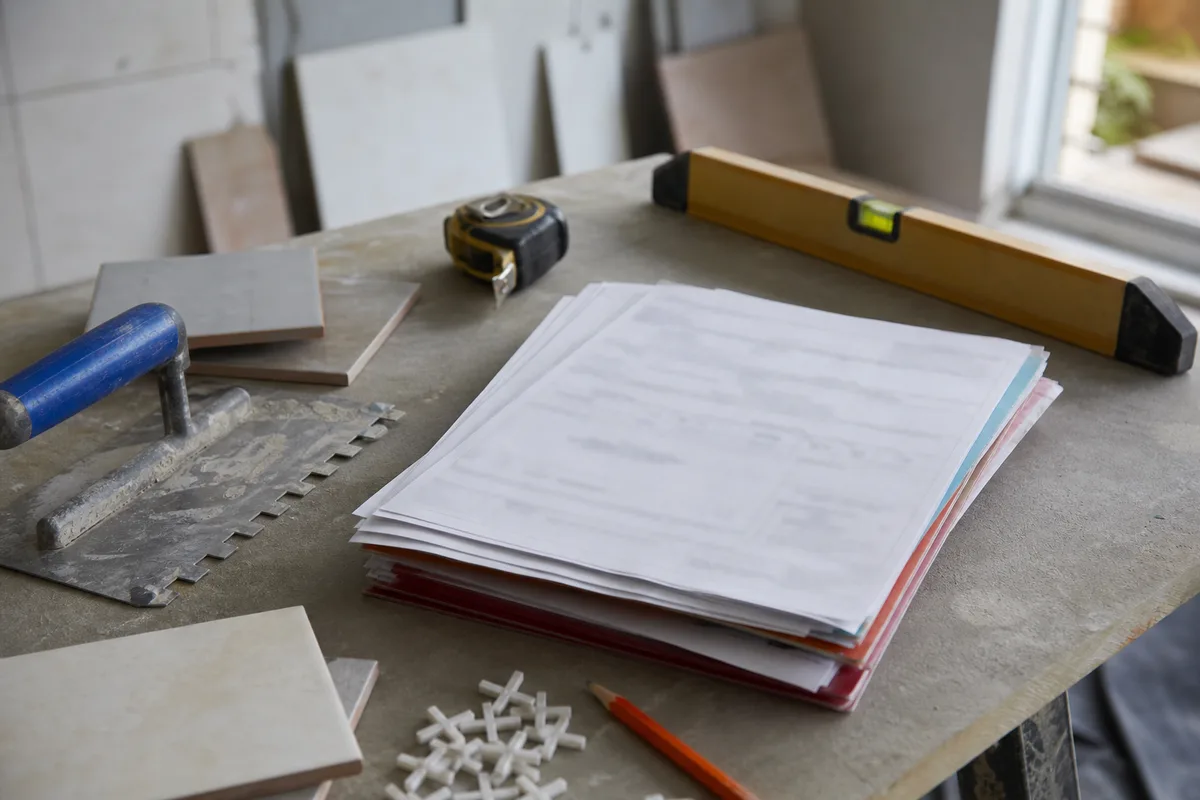Documents administratifs de chantier posés sur un plan de travail avec outils de carreleur