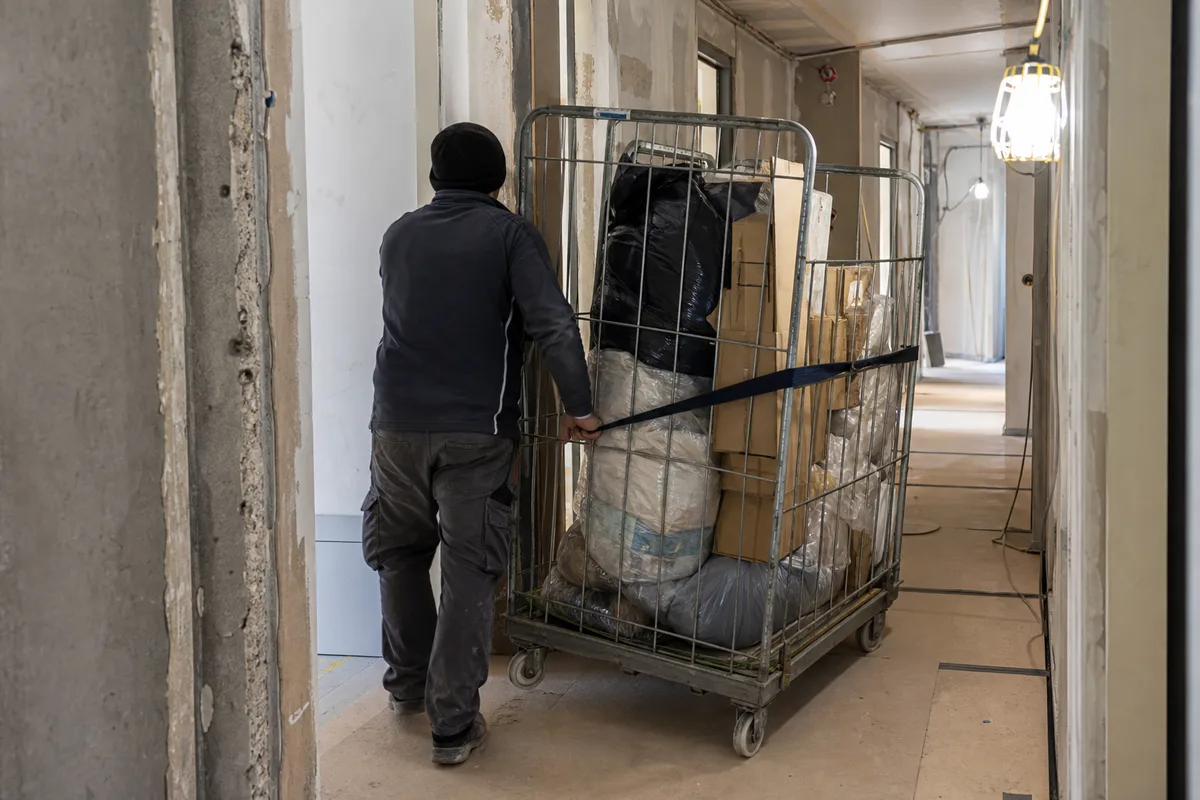 Roll conteneur grillagé chargé de matériaux poussé dans le couloir d&rsquo;un bâtiment en rénovation